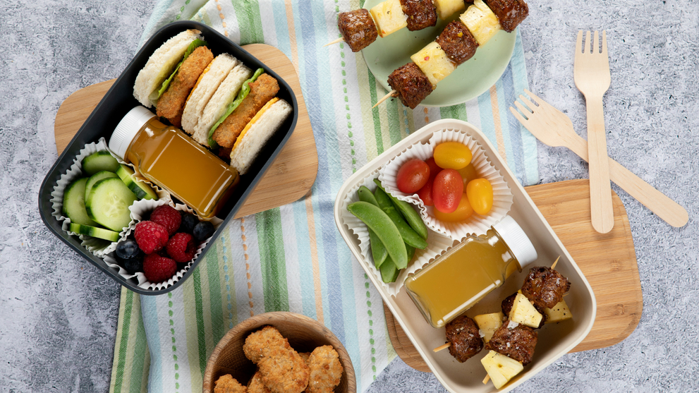 Packed cold lunch boxes with sandwiches, fresh fruit, vegetables, and protein skewers